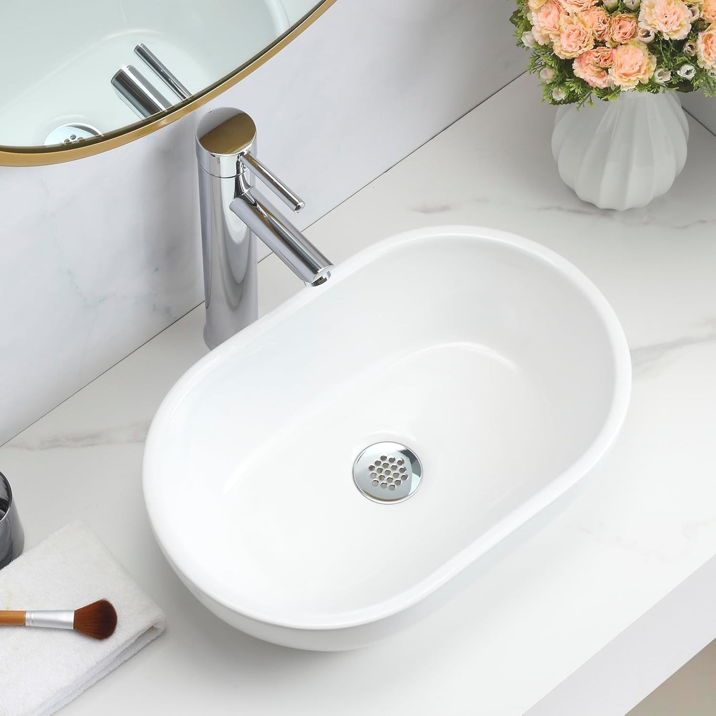 Gloss white oval counter top basin on a marble vanity with a gold-framed mirror.