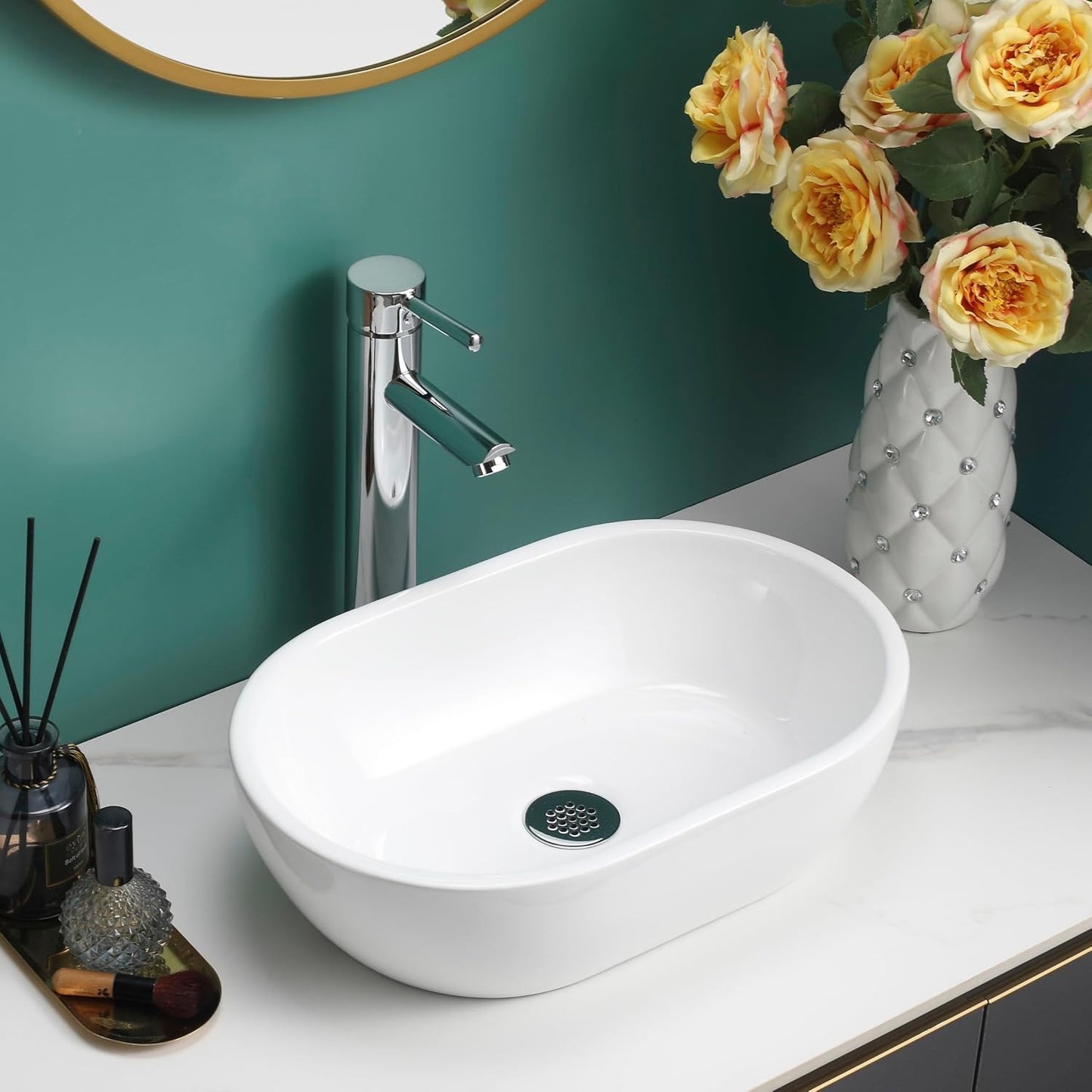 Gloss white oval counter top basin on a white countertop with gold decor and flowers.