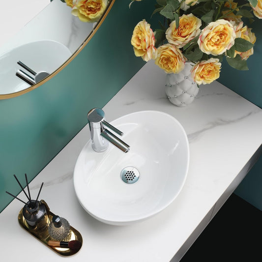 Gloss white oval counter top basin on a white marble countertop with flowers and a mirror.