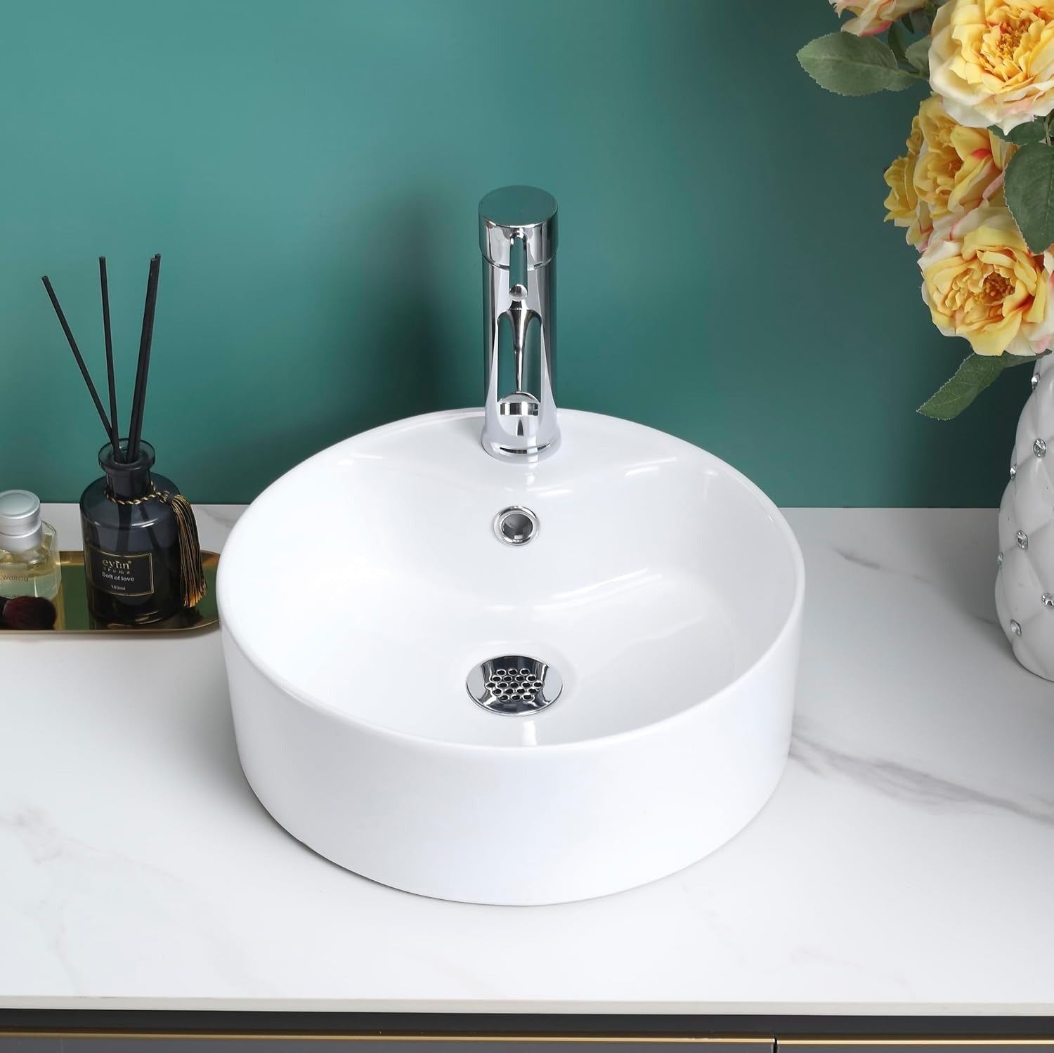 Gloss white round counter top basin on a white countertop with gold decor and flowers.